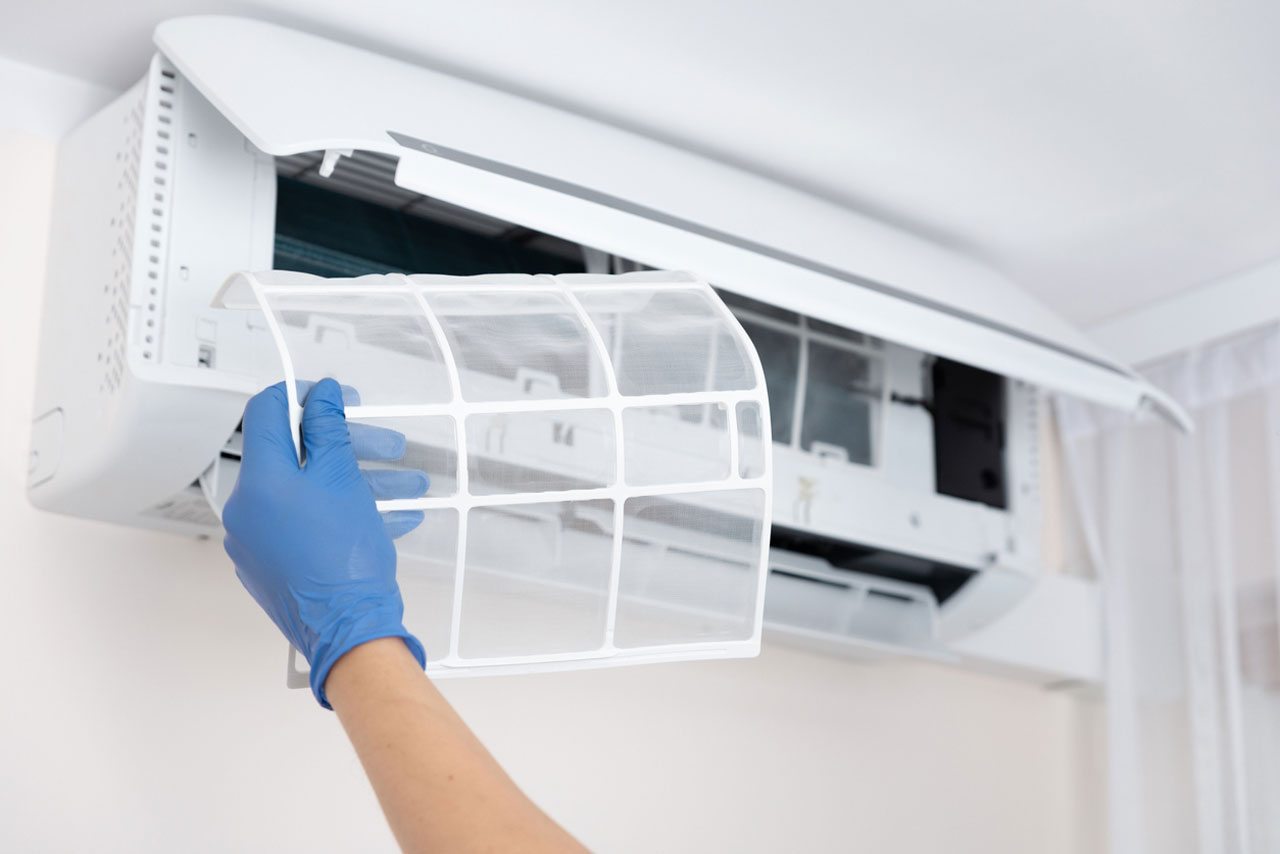 Professional wearing blue gloves, removing a clean air filter from an air conditioner.