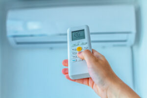 Close-up of a hand holding a remote control aimed at changing the temperature of an air conditioner.