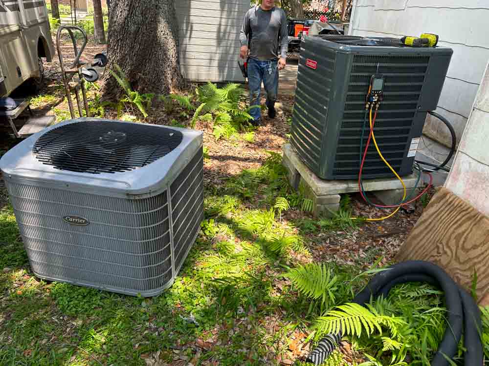 Technicians actively working on servicing outdoor Goodman and Lennox air conditioning units in a residential backyard.
